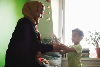 Mother putting gloves on son's hand in bedroom