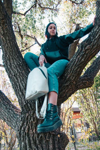 Young woman sitting on tree trunk holding a backpack
