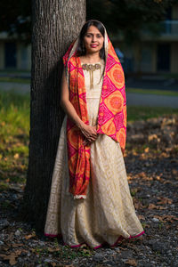 Portrait of young woman standing on tree trunk