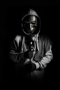 Portrait of young man holding camera against black background