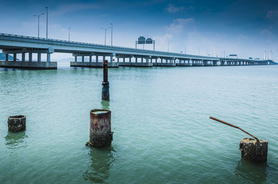 Abandoned metallic posts by bridge over sea against sky