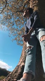 Low angle view of man standing by tree against sky