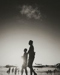 Silhouette friends standing on beach against clear sky