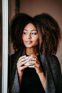 Thoughtful woman drinking coffee while looking through window at home