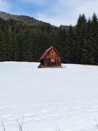 Cottage amidst snow covered landscape by trees against sky 