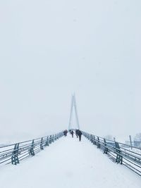 People on snow covered footbridge against sky