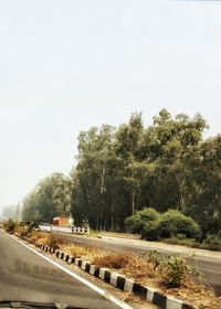 Road by trees against clear sky