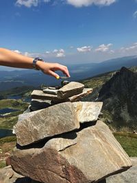 Cropped hand of woman stacking rocks against mountains during sunny day