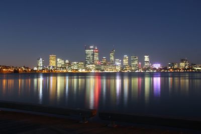 Sea by illuminated buildings against clear sky at night