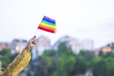 Cropped hand of woman holding rainbow flag against sky