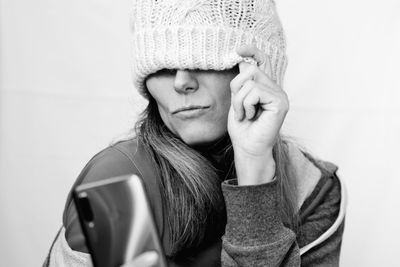 Portrait of young woman holding hat against white wall