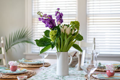 Pretty spring table setting with fresh flower bouquet as a centerpiece in dining room 