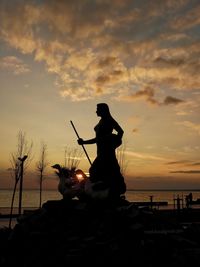 Silhouette man statue by sea against sky during sunset