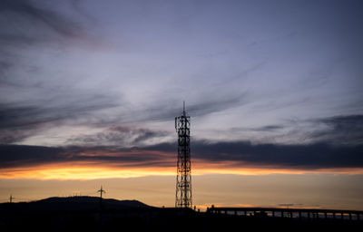 Silhouette communications tower against dramatic sky during sunset