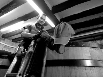 Low angle view of man looking at cap on his feet against illuminated light on ceiling