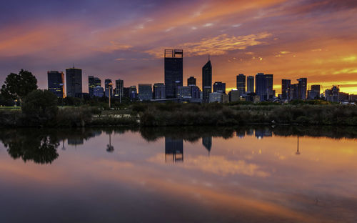 Reflection of buildings in city against sky during sunset