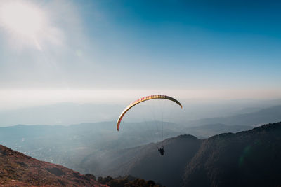 Person paragliding over mountains against sky