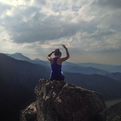 Rear view of woman sitting on cliff against cloudy sky