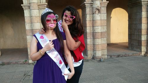 Portrait of smiling females with props while standing against building