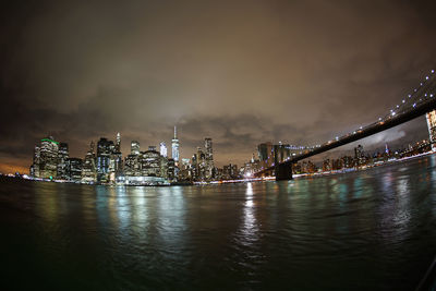 Illuminated bridge over river against buildings at night