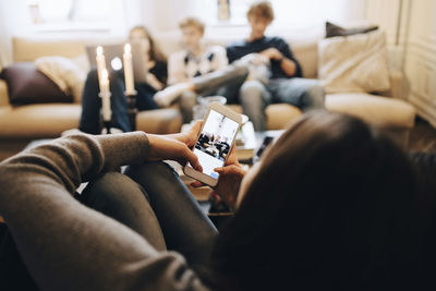 Girl photographing friends sitting on sofa at home