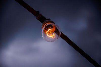 Low angle view of illuminated light bulb against sky