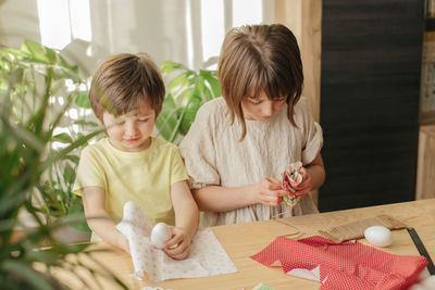 A boy and a girl, sibling are crafting easter eggs from cloth in the shape of a bunny. 