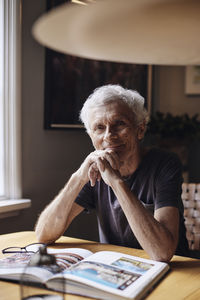 Portrait of smiling senior man with hand on chin sitting at home