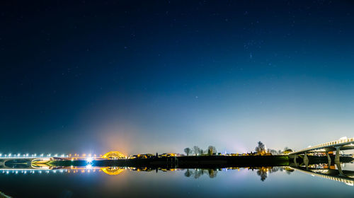 Reflection of illuminated bridge over river against sky at night