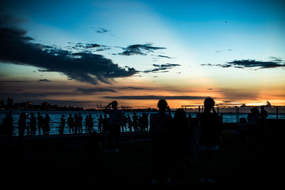 Silhouette people on beach against sky during sunset