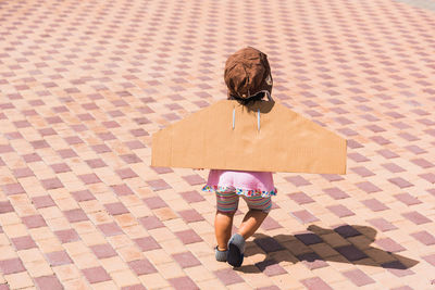 Rear view of baby girl wearing costume wings on footpath