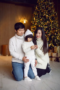 Beautiful korean family with their daughter are sitting at home by the christmas tree