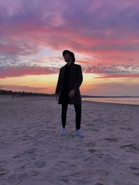 Rear view of man standing at beach against sky during sunset