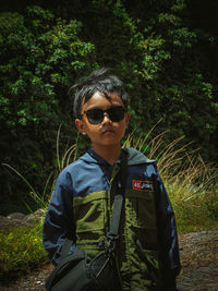 Portrait of young man wearing sunglasses standing in forest