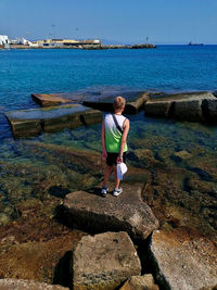 Boy on rock by sea against sky