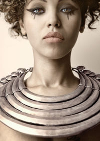 Close-up portrait of woman wearing necklace against wall