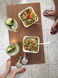 Low section of couple standing by noodles and lemonades on wooden table at floor