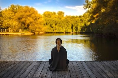 Young woman sitting on jetty by lake against sky