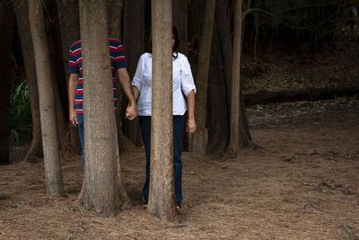 Couple standing behind tree trunks in forest