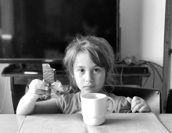 Portrait of serious girl holding chocolate while sitting by mug at table