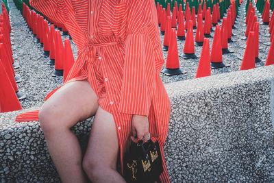 Midsection of woman sitting on retaining wall against traffic cones