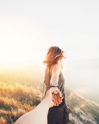 Woman holding hand on mountain against sky during sunset