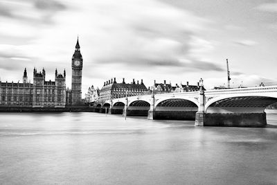 View of clock tower bridge in city against cloudy sky