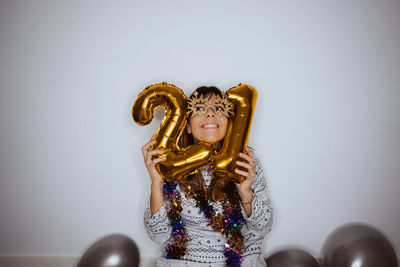 Smiling woman holding balloons looking up while sitting against wall at home