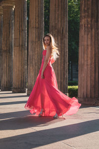 Full length side view of young woman in pink evening gown walking at colonnade