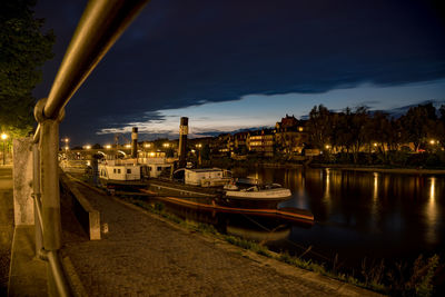 Boats moored on river by illuminated buildings in city at night