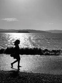 Side view of silhouette girl walking on beach against sky