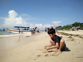 Side view of cute boy playing with sands at beach during sunny day