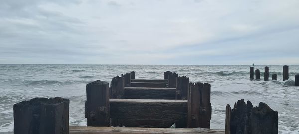 Wooden posts on sea against sky