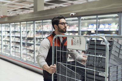 Sales clerk pushing cart with plastic crates at refrigerated section in supermarket